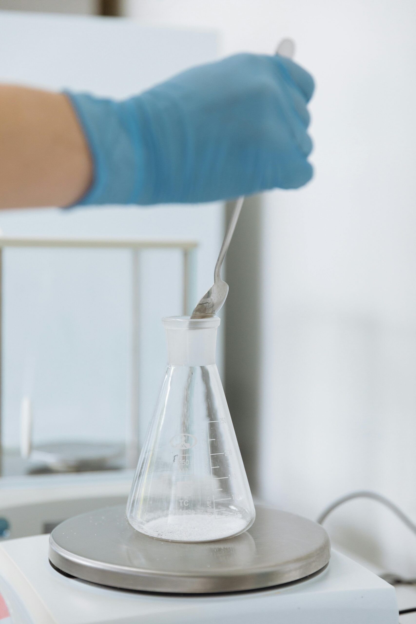 Close-up of a scientist's hand mixing chemicals in a laboratory Erlenmeyer flask using a spoon.